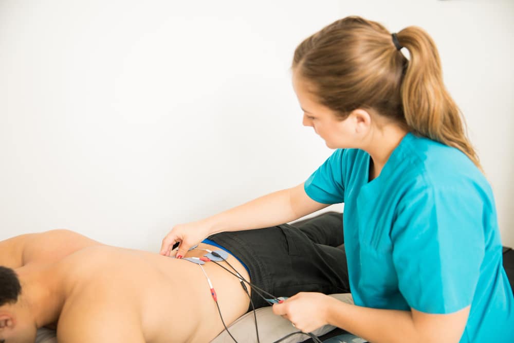 female physical therapist positioning electrodes customer lower back muscle treatment clinic